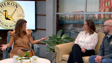 Un entrevistador sentado en una silla y entrevistando a dos personas que están sentadas en un sofá.